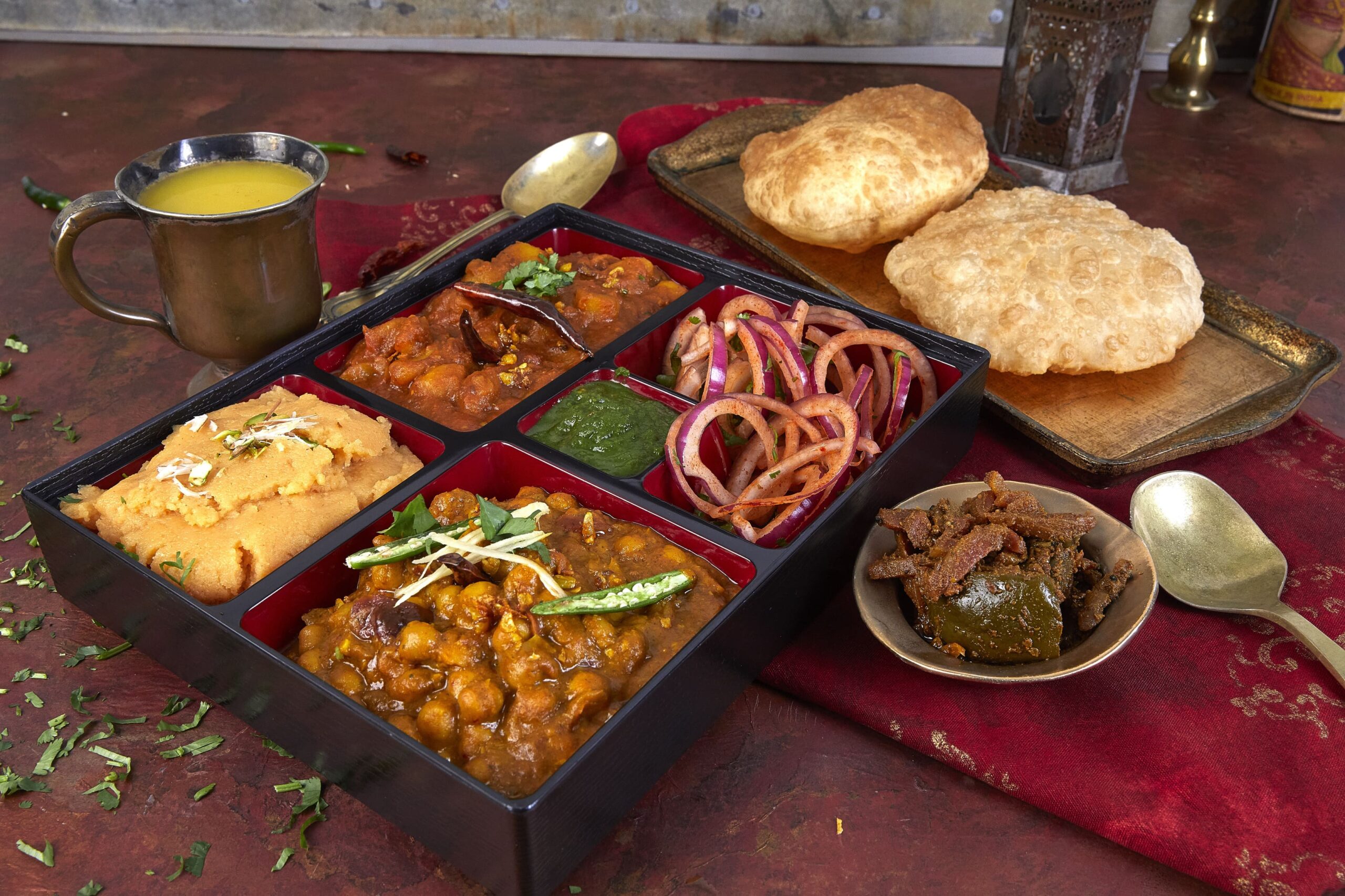 Bombay Bento Menu featuring Chole Bhature Bento with fluffy bhature, spicy chole, aloo ki sabzi, sooji ka halwa, mint sauce, and pickle.